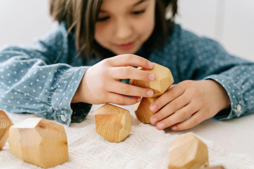 pexels-photo-8504538-8504538 A young girl stacking wooden blocks, engaging in mindful play for cognitive development.